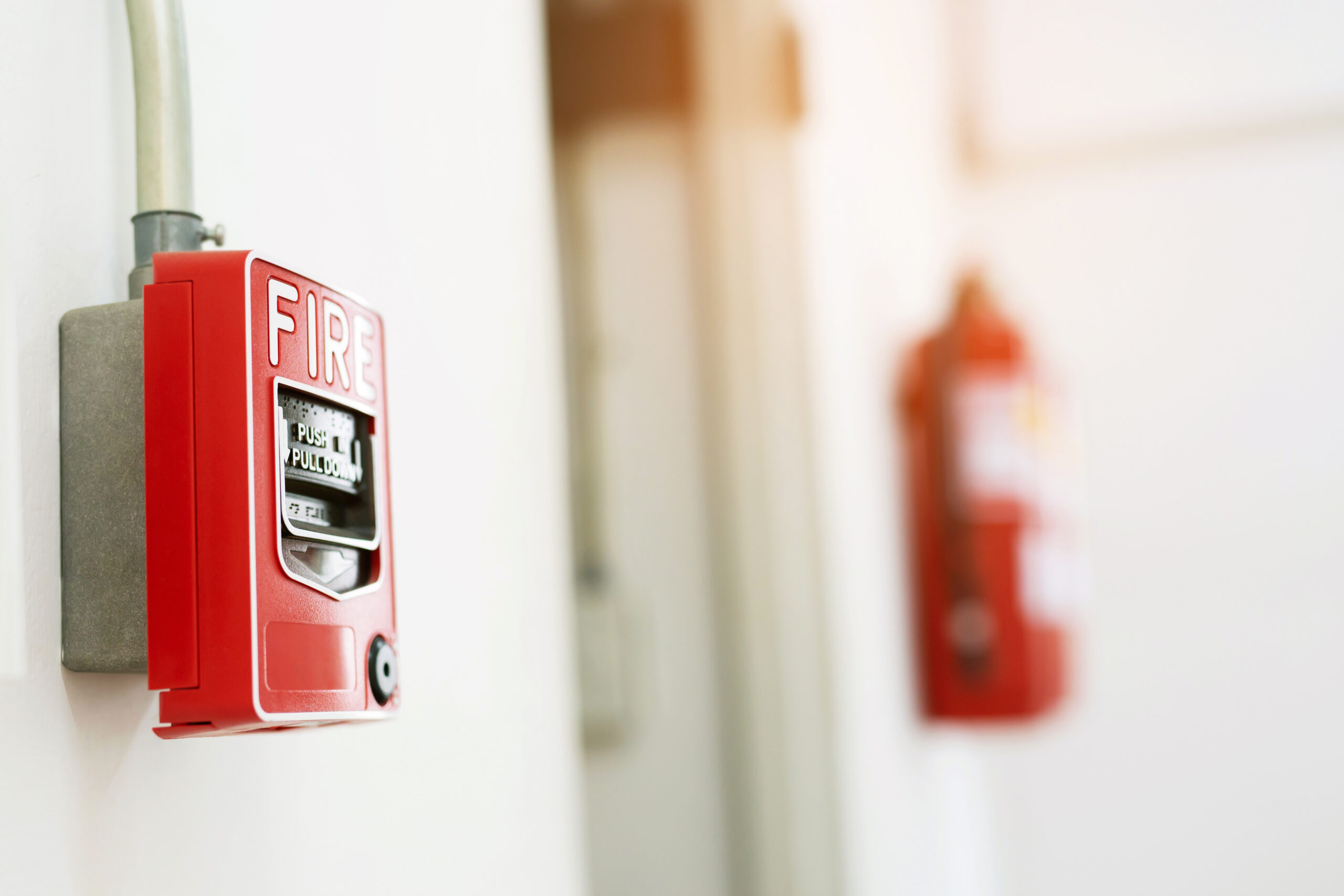 Manual pull fire alarm switch safety system box installed and fire extinguisher on white wall background.